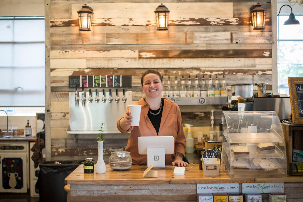A worker handing out a cup of coffee with a smile on her face