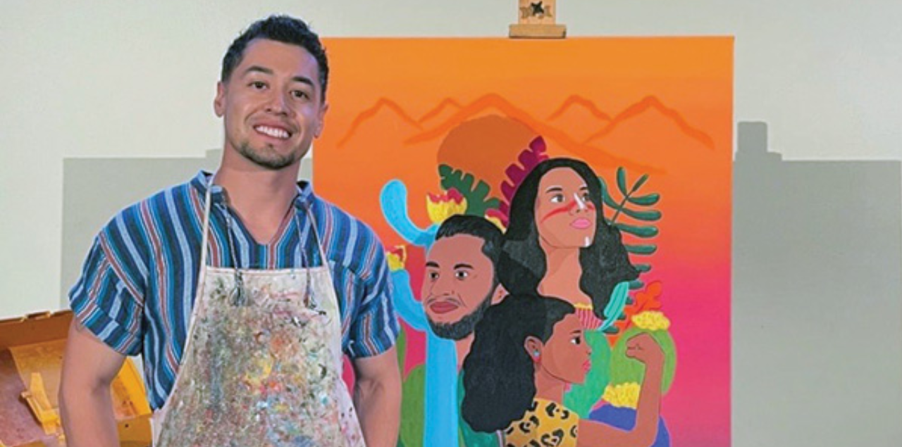 Julio “Juls” Mendoza standing in front of a colorful work of art he painted.