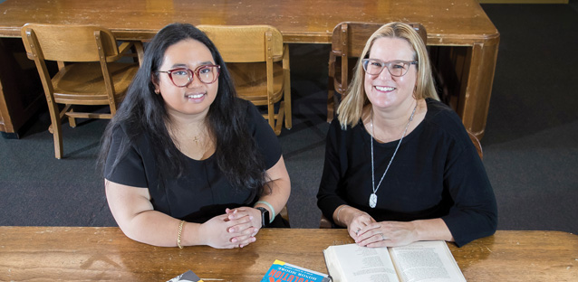 Two women sitting at a wooden table and smiling