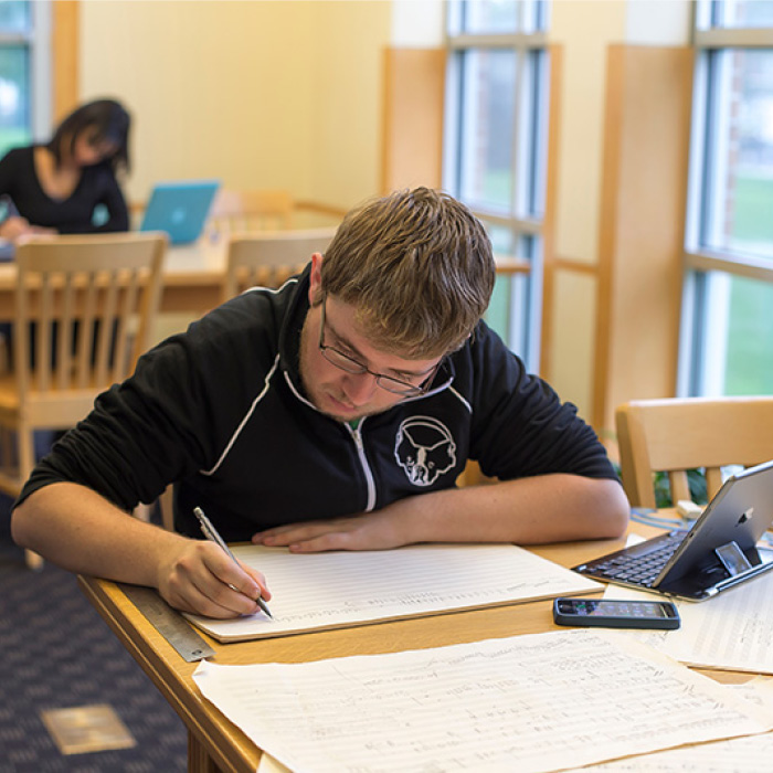 Student writing on staff paper at a table in Skinner Music Library.
