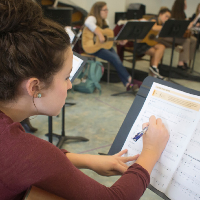 Student writing in a method book during a music education class.