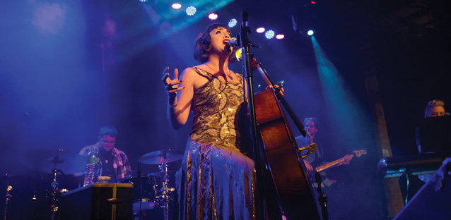 Neyla Pekarek singing in a microphone holding a chello