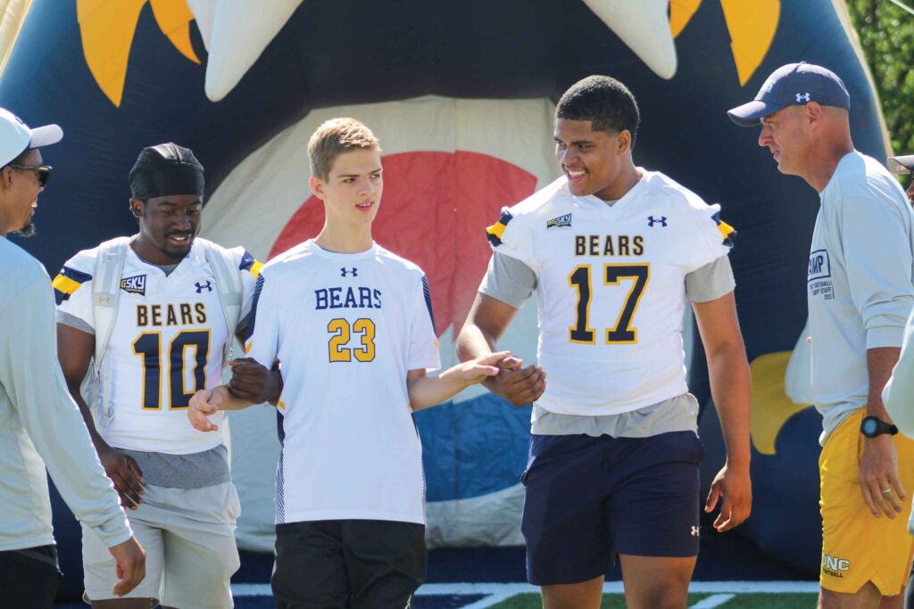 UNC athletes helping a student walk onto the football field.