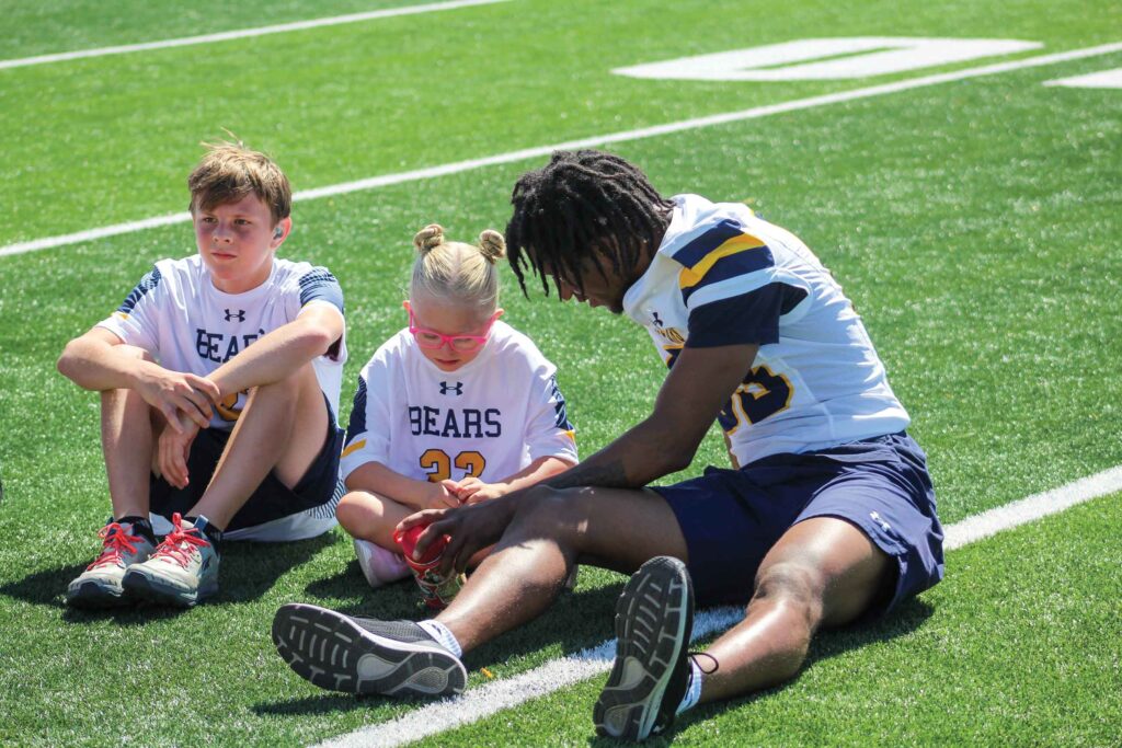 Two camp participants sitting on the football field with a UNC athlete.
