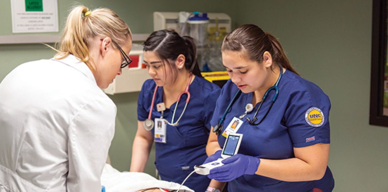 Two UNC nursing students and a faculty member conducting clinical research in a hospital room.