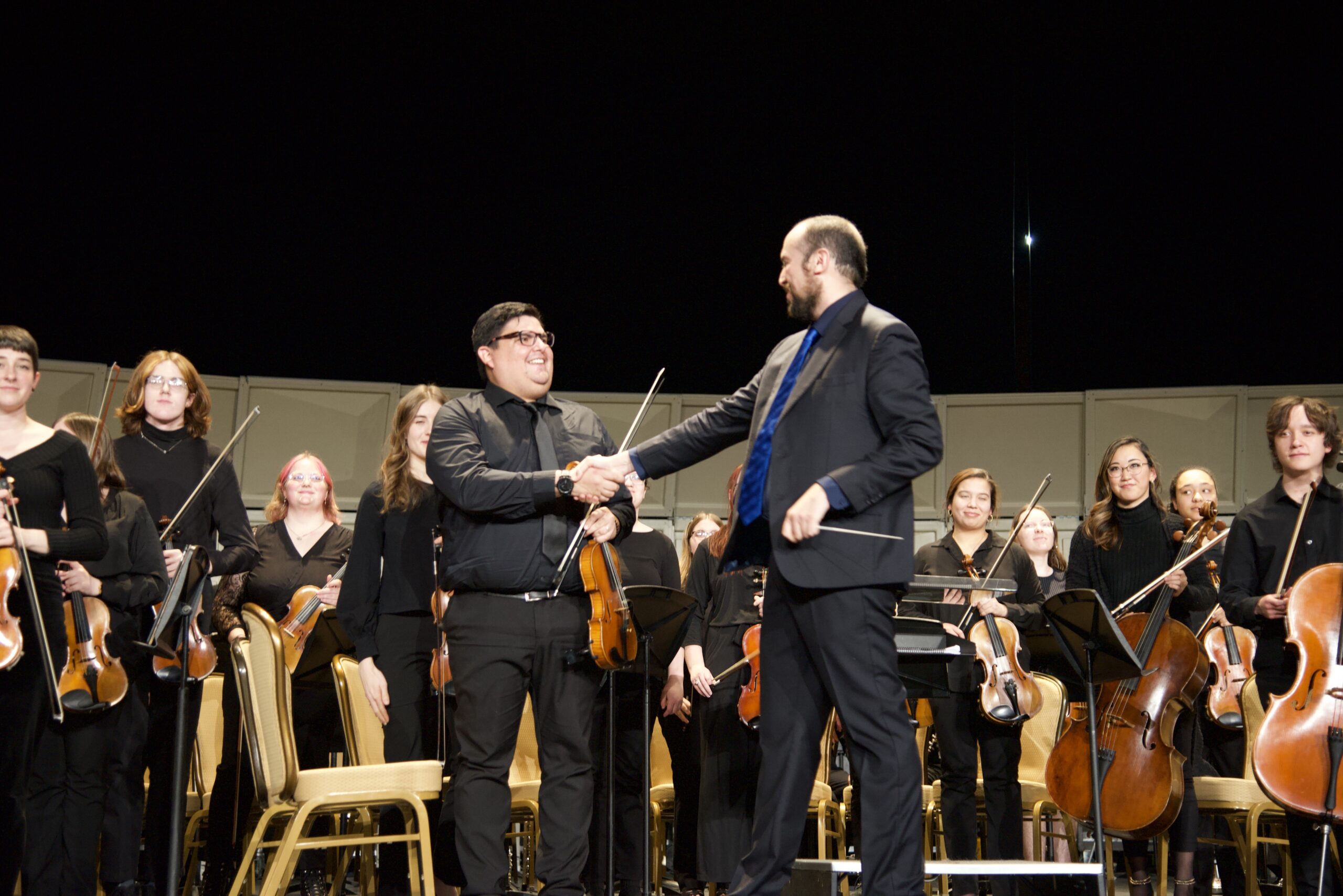 Orchestra conductor Andrés Felipe Jaime shaking hands with the concert master during applause.