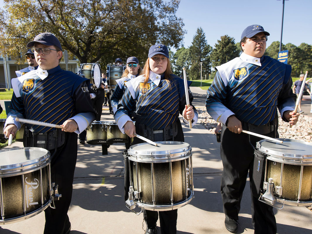 Three UNC students playing on the drumline in the Pride of the Rockies Marching Band.