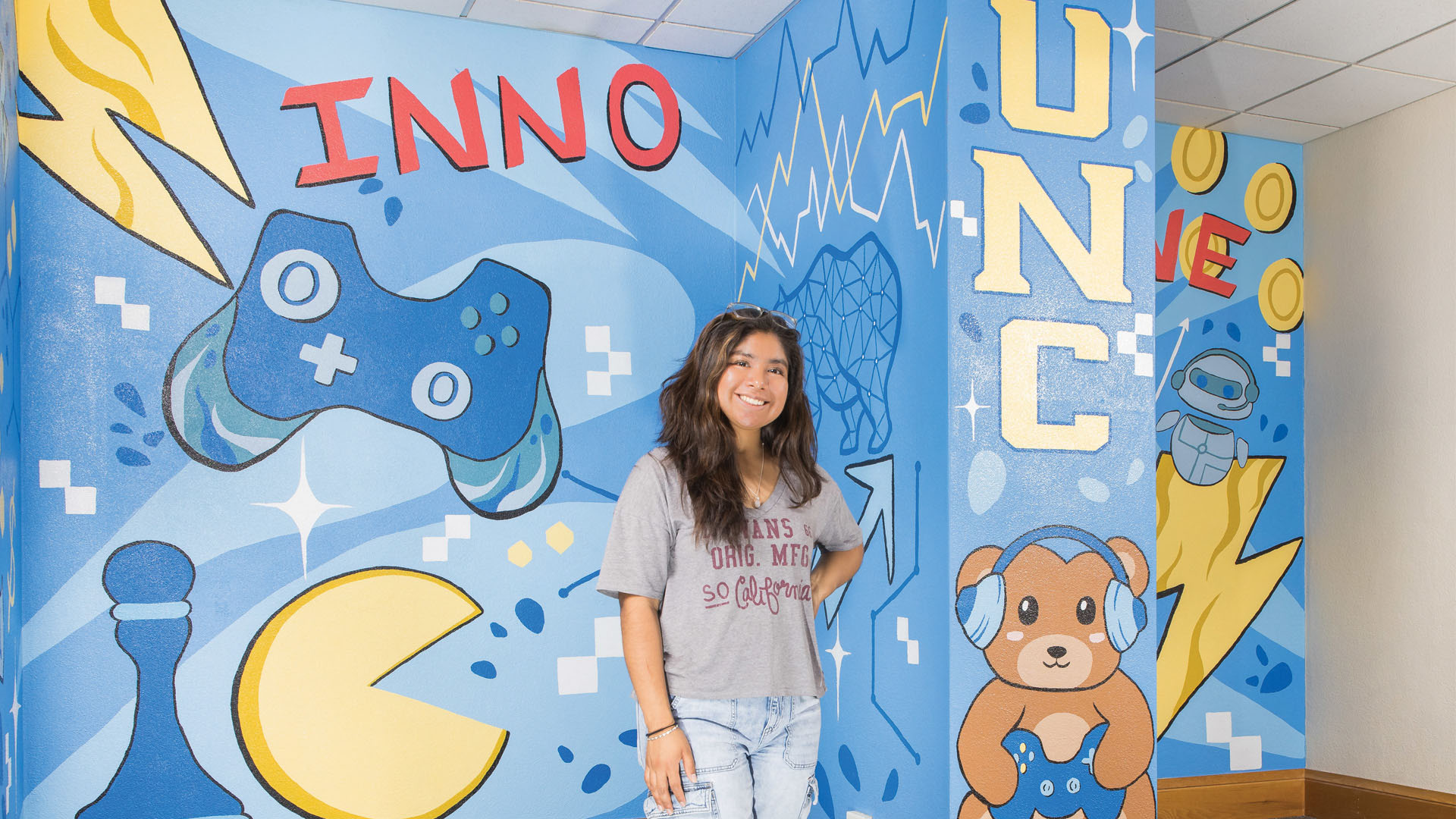 Raquel Nunez standing in front of the mural she painted in various colors of blue and yellow