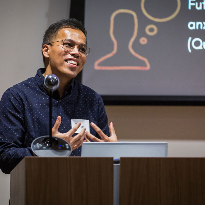 Graduate student presenting research at podium with screen behind.