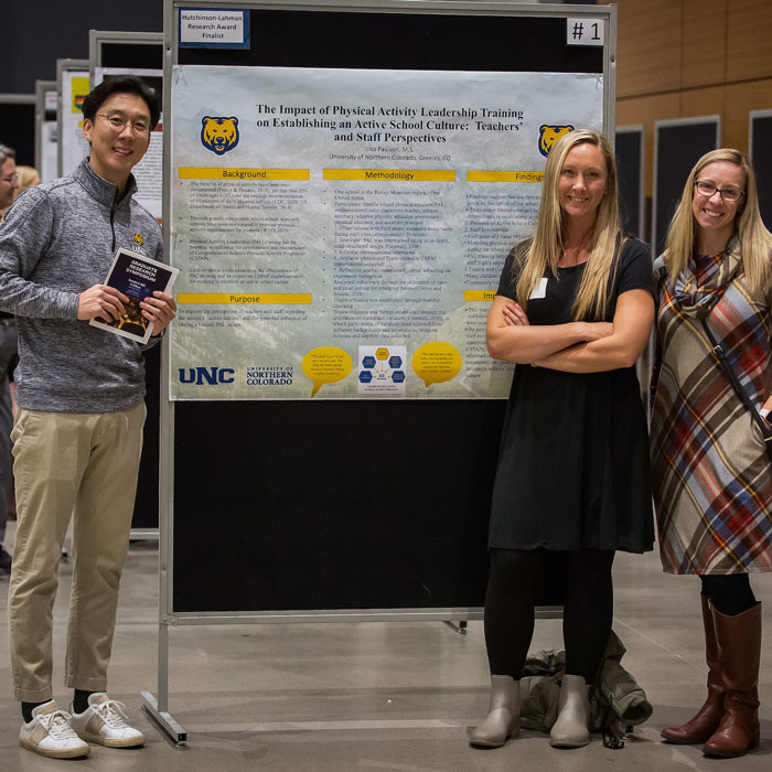 Three graduate students in front of a research poster.