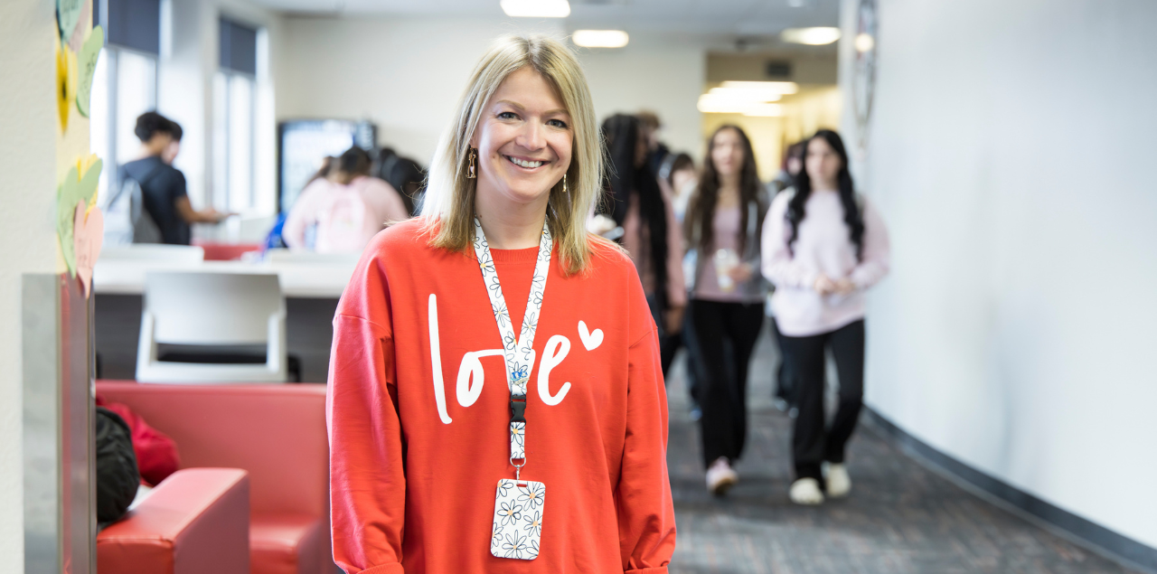 A teacher in a red shirt standing in the hallway of a high school.