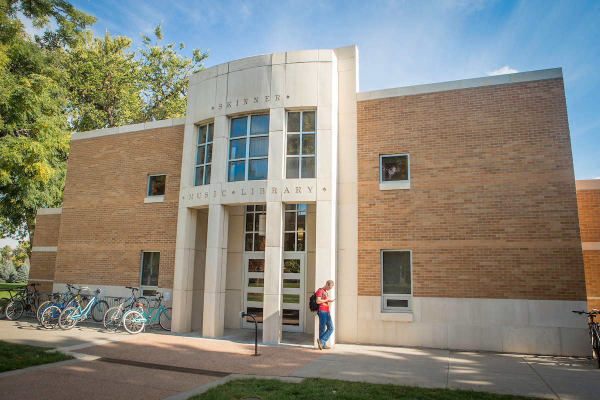 Exterior of Michener Library, with a student standing outside. The sun is shining.