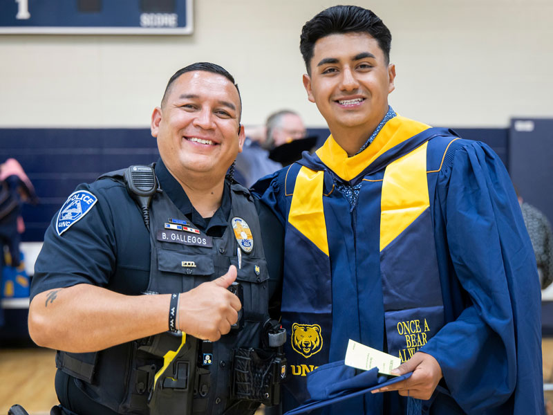 Graduating graduate student in regalia, standing next to a UNC police officer who is giving a thumbs up.