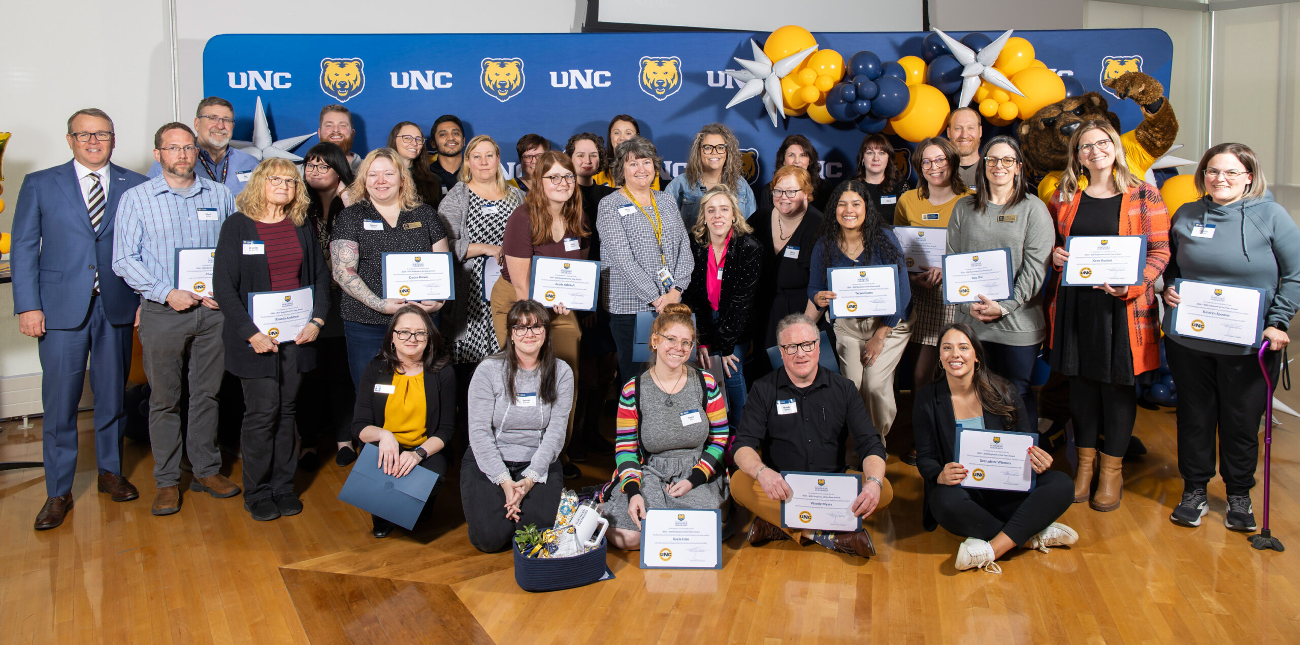 A group of UNC staff posing in front of a UNC backdrop inside