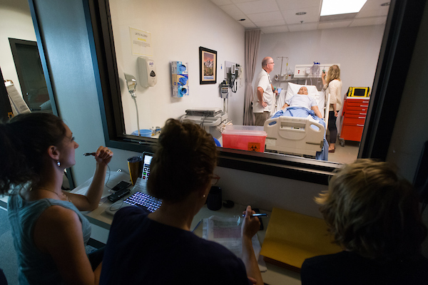 Professors monitoring students within a observation room for a nursing lab simulation