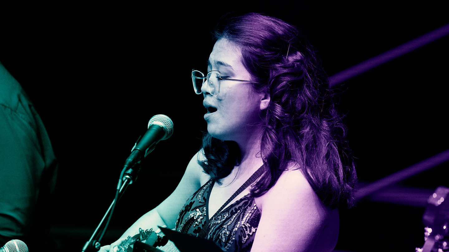 UNC Arts season photo of woman singing into a microphone and playing guitar.