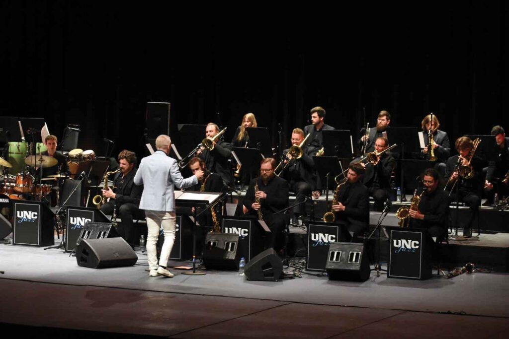 A band of UNC students dressed in black playing their instruments onstage.