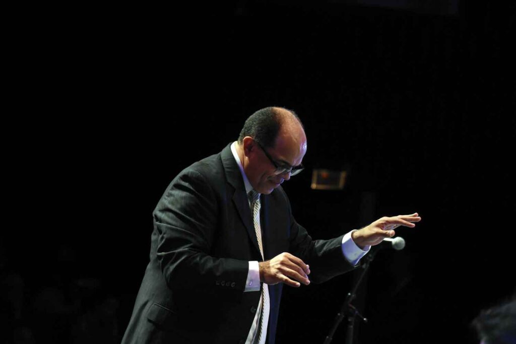 A man in a suit conducting a band onstage.