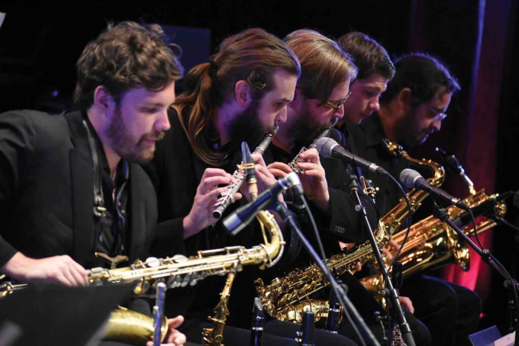 A group of students playing brass and woodwind instruments onstage.