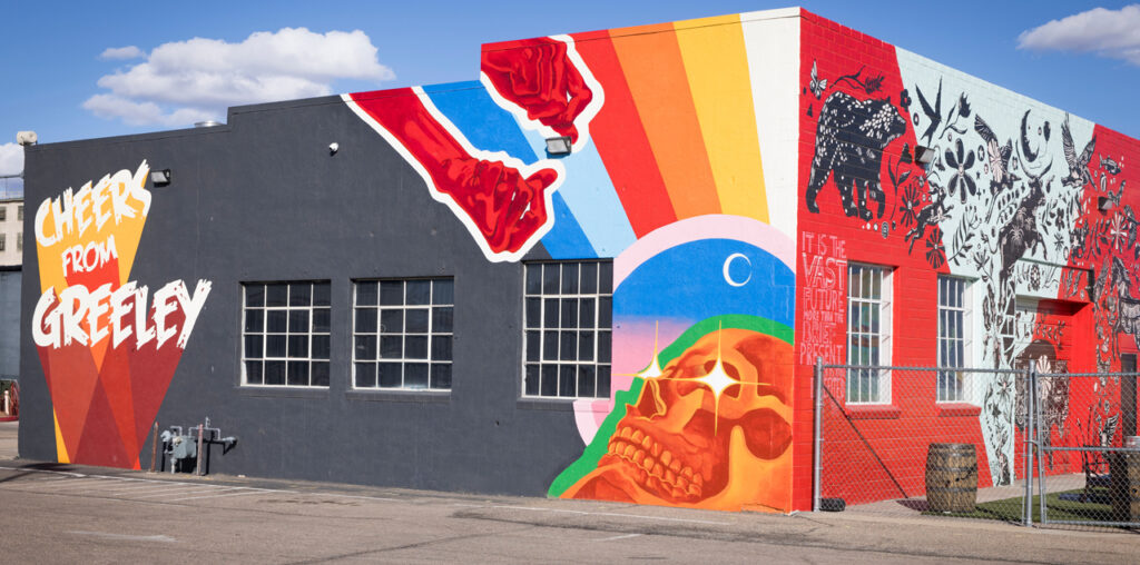 A colorful mural of a skull with shining eyes and two hands reaching down.