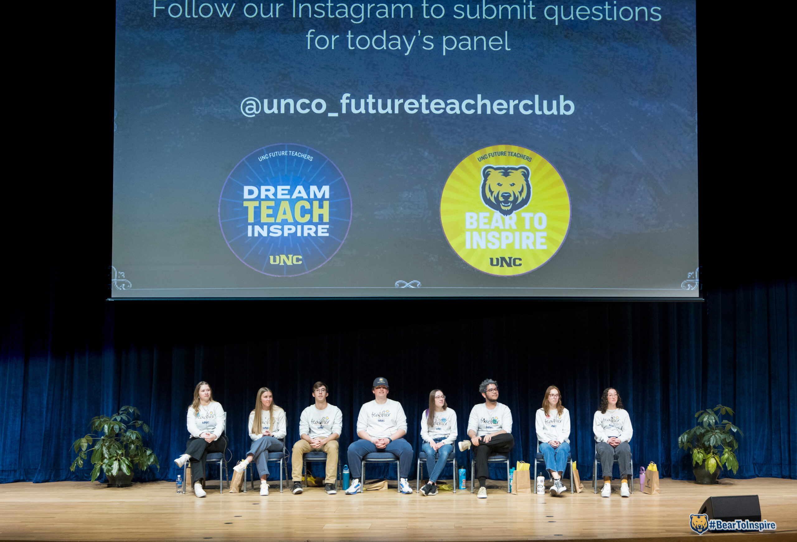 UNC students on stage with a screen showing the Future Teacher Club Instagram handle and logos reading “Dream Teach Inspire” and “Bear to Inspire.”