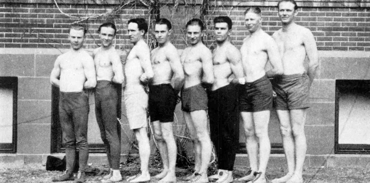 Black and white photo of a line of wrestlers standing from tallest to shortest.