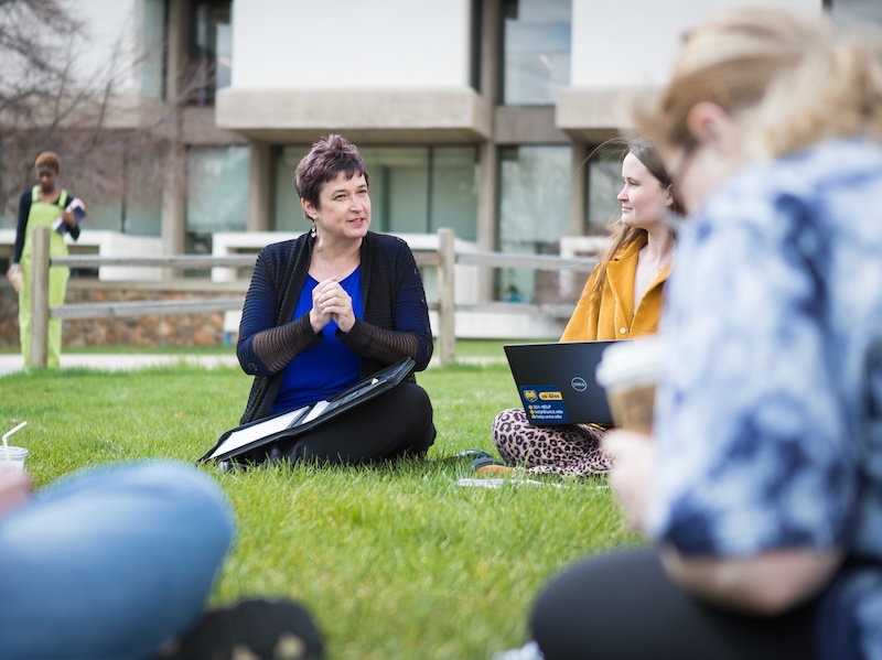 Group of students outside on grass with laptops in class setting.