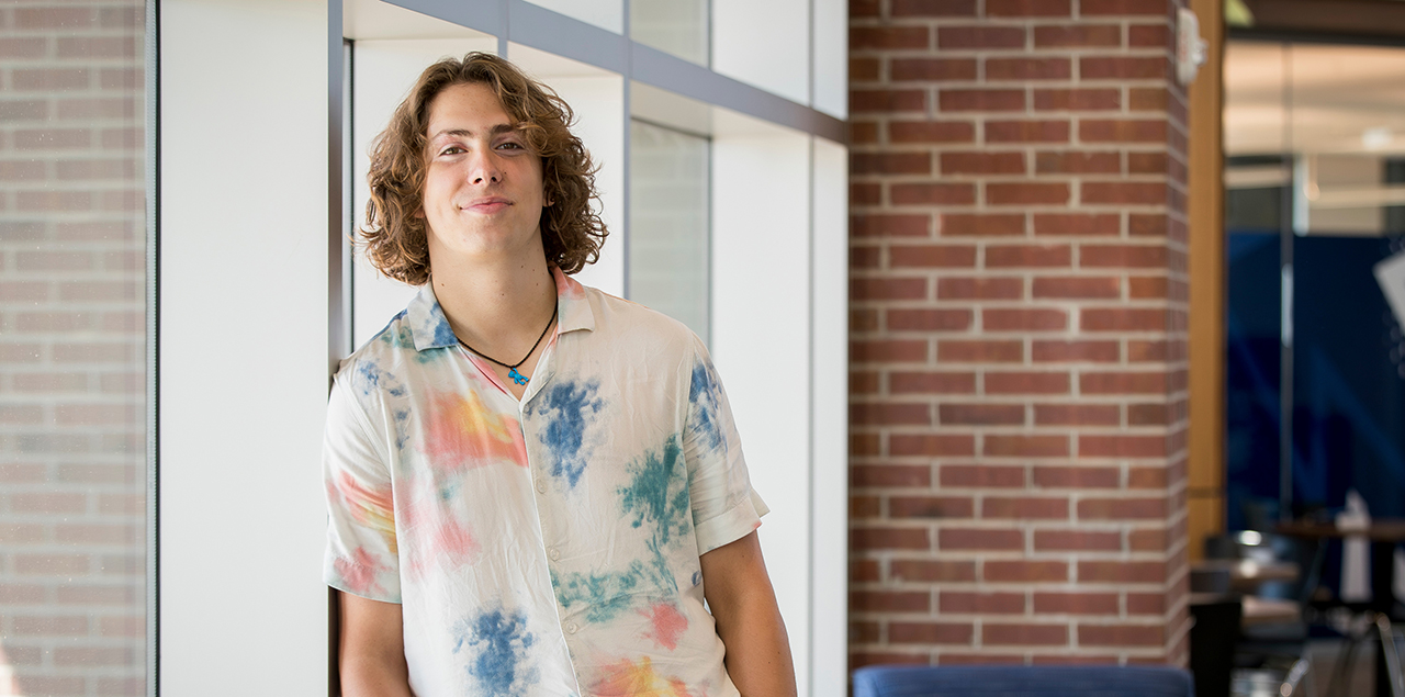 Image of Parker Coffelt leaning against a glass wall in campus building