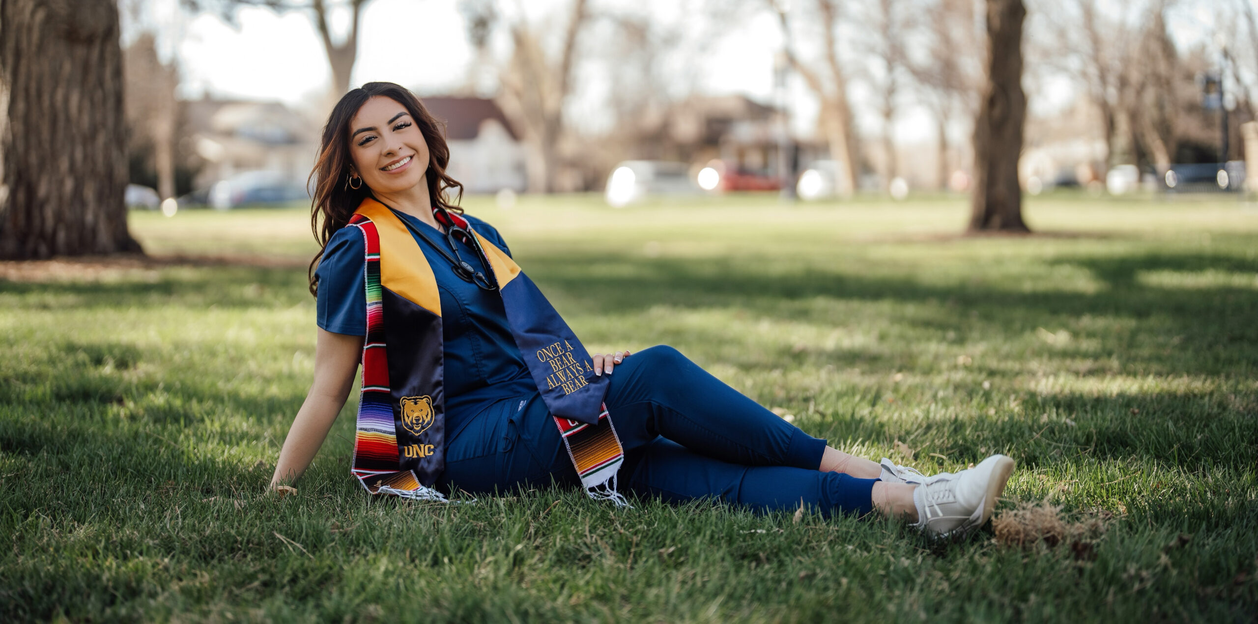 Image of Rosemary Gonzalez sitting on grass with her graduation gold stole