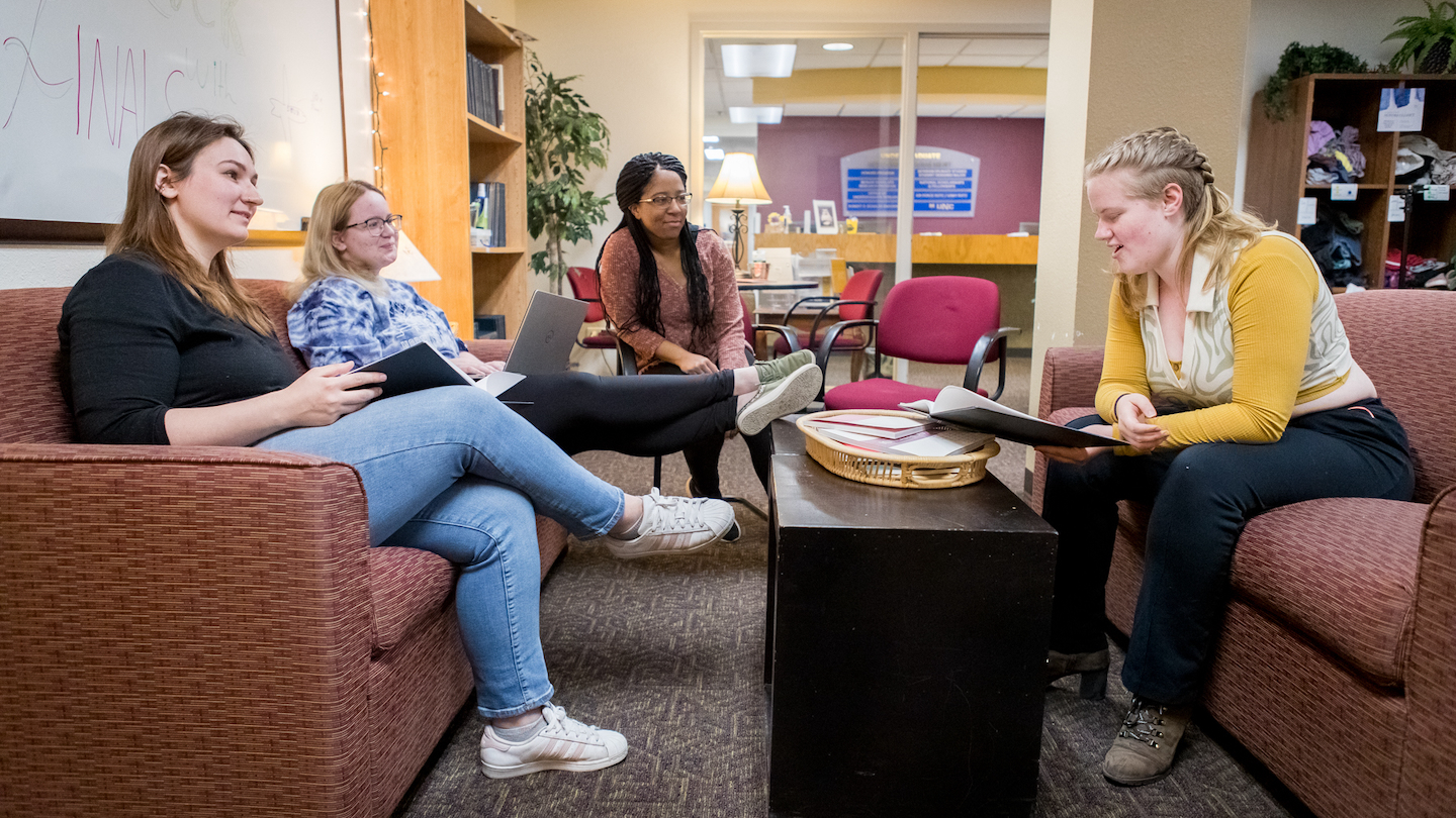 Group of three students with graduate assistant reviewing materials in U-Engage Lounge.