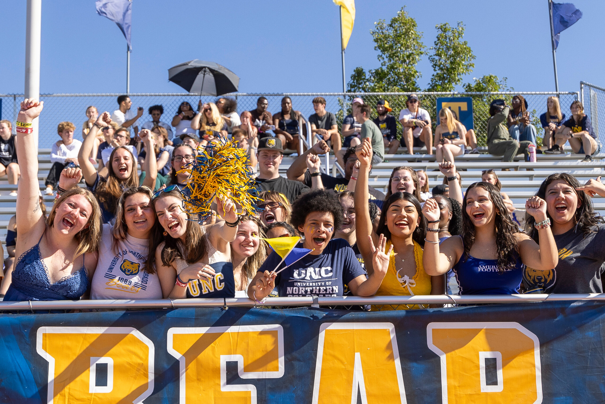 A group of students wearing UNC merch cheering in the student section of the bleachers