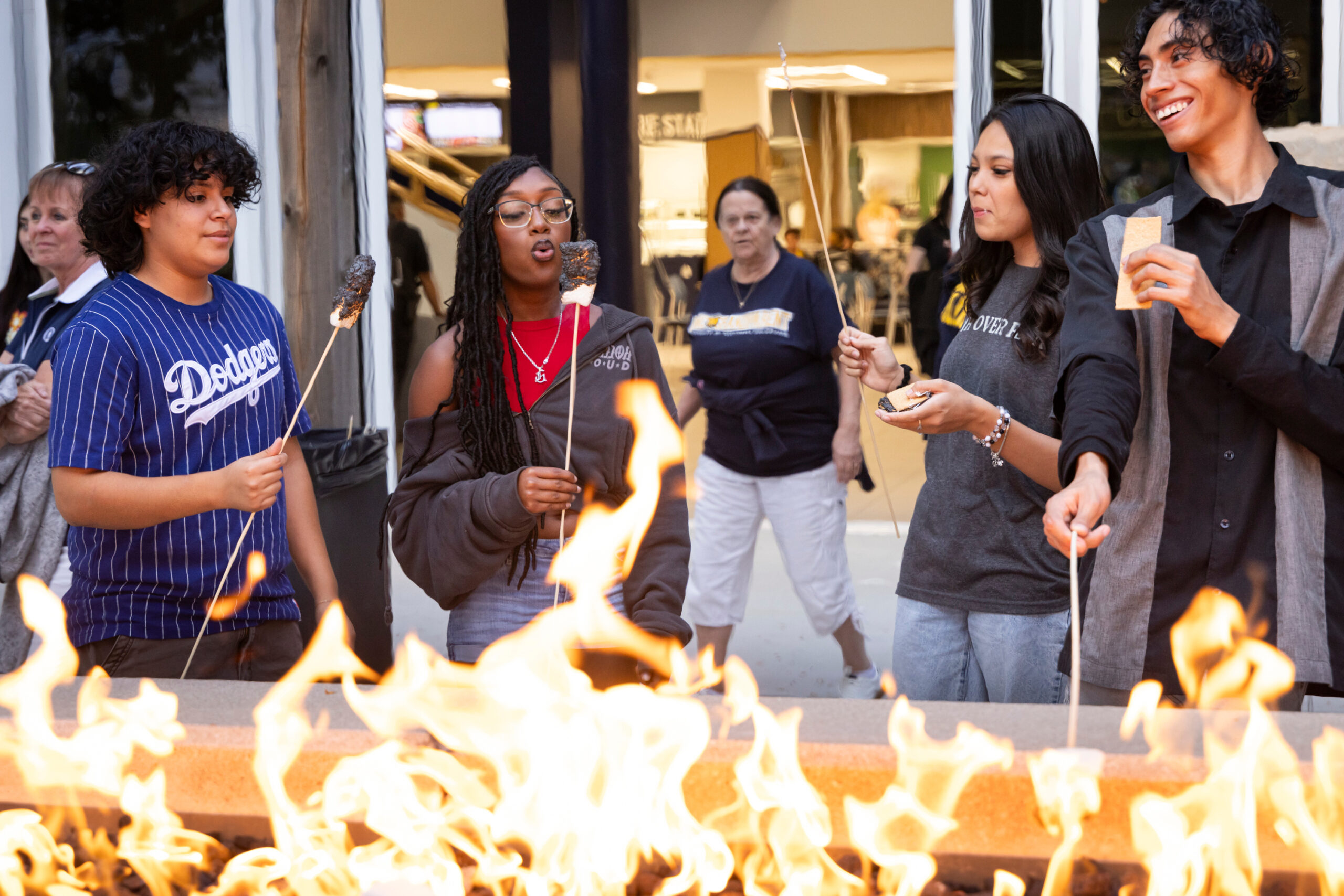A group of students roasting marshmallows in front of a firepit