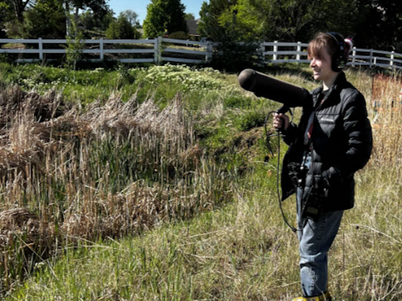 Student holding a large microphone in a field.