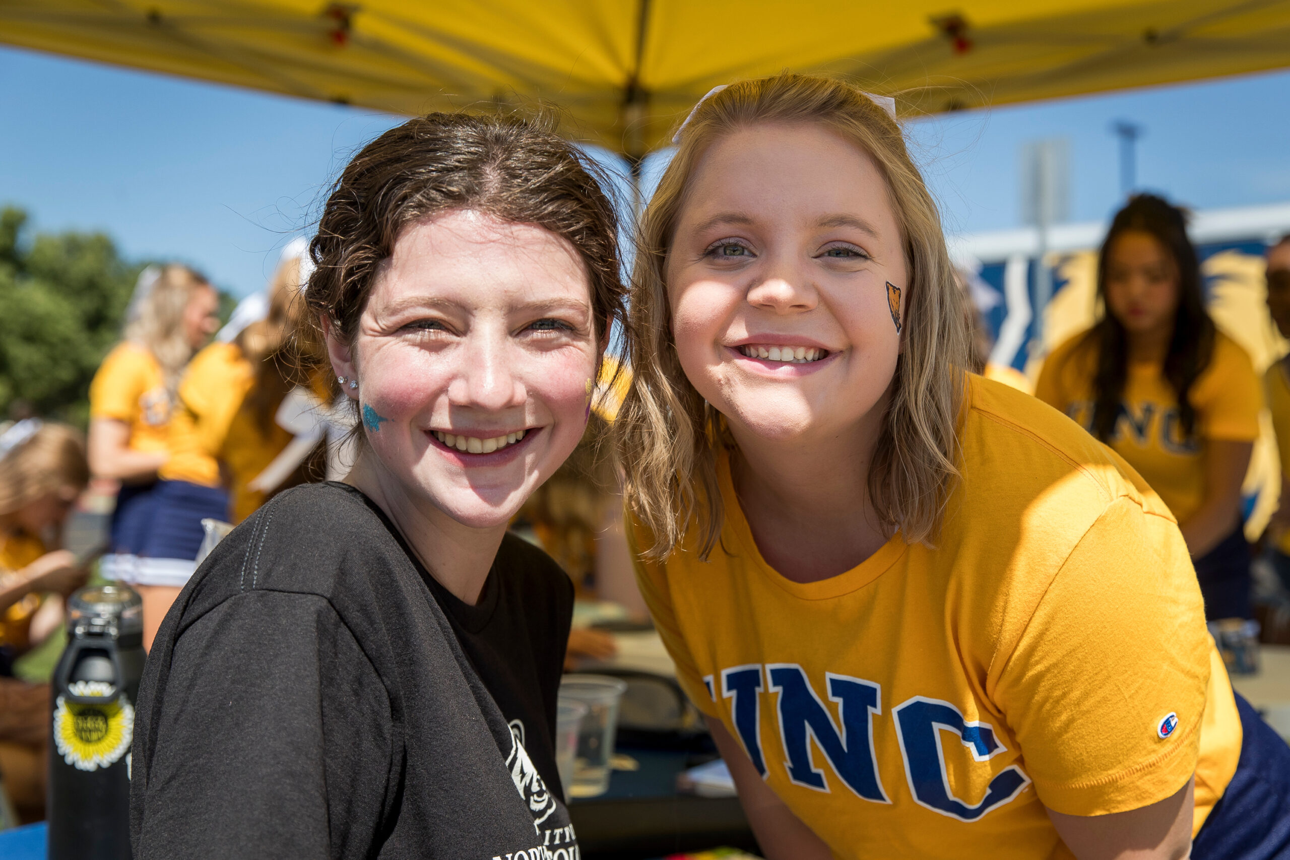 Two students next to each other smile at the camera, UNC tattoos on their cheeks.