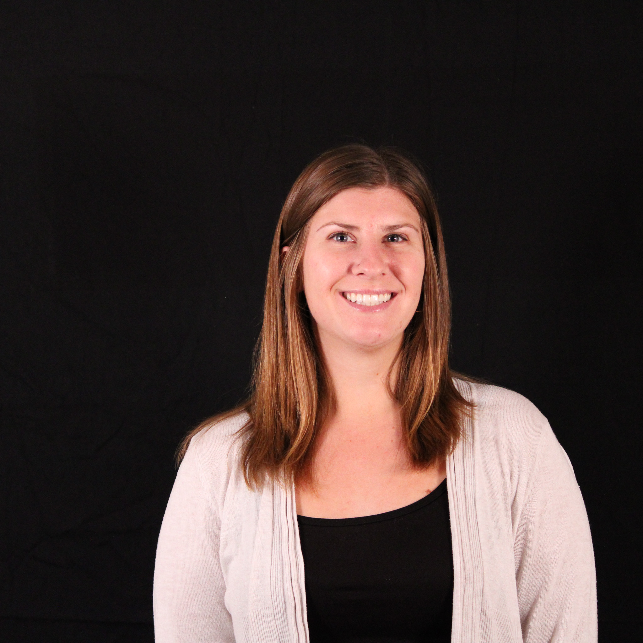 A woman smiling, dressed in a white sweater, against a black background