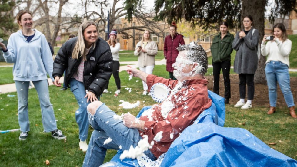 Students throw a pie at a staff member for a fundraising event.