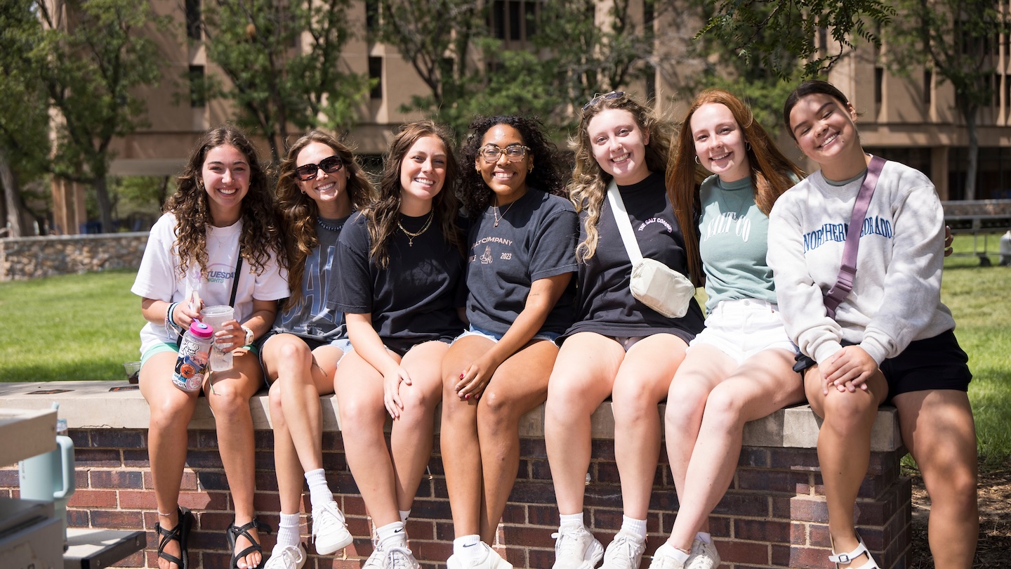 Female college students sitting on brick wall smiling