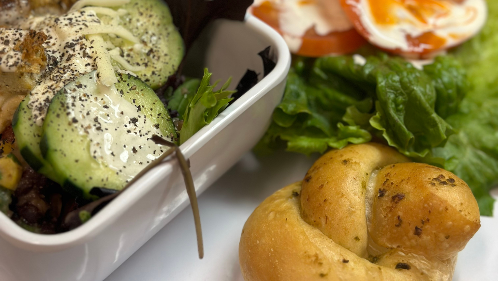 A salad, a garlic knot, and a sandwich sit on a tray