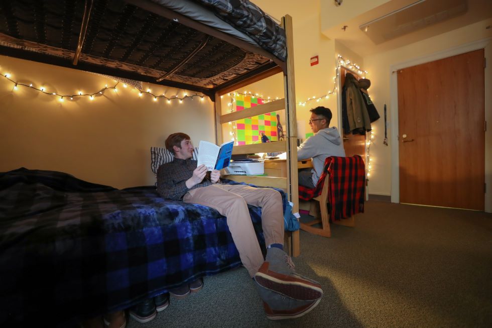 Students lounging in room one on the bed reading and the other at their desk