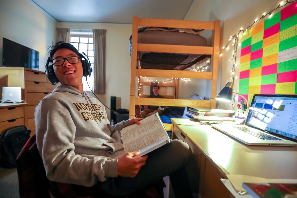 Student with headphones at his desk with book at lookin over his shoulder
