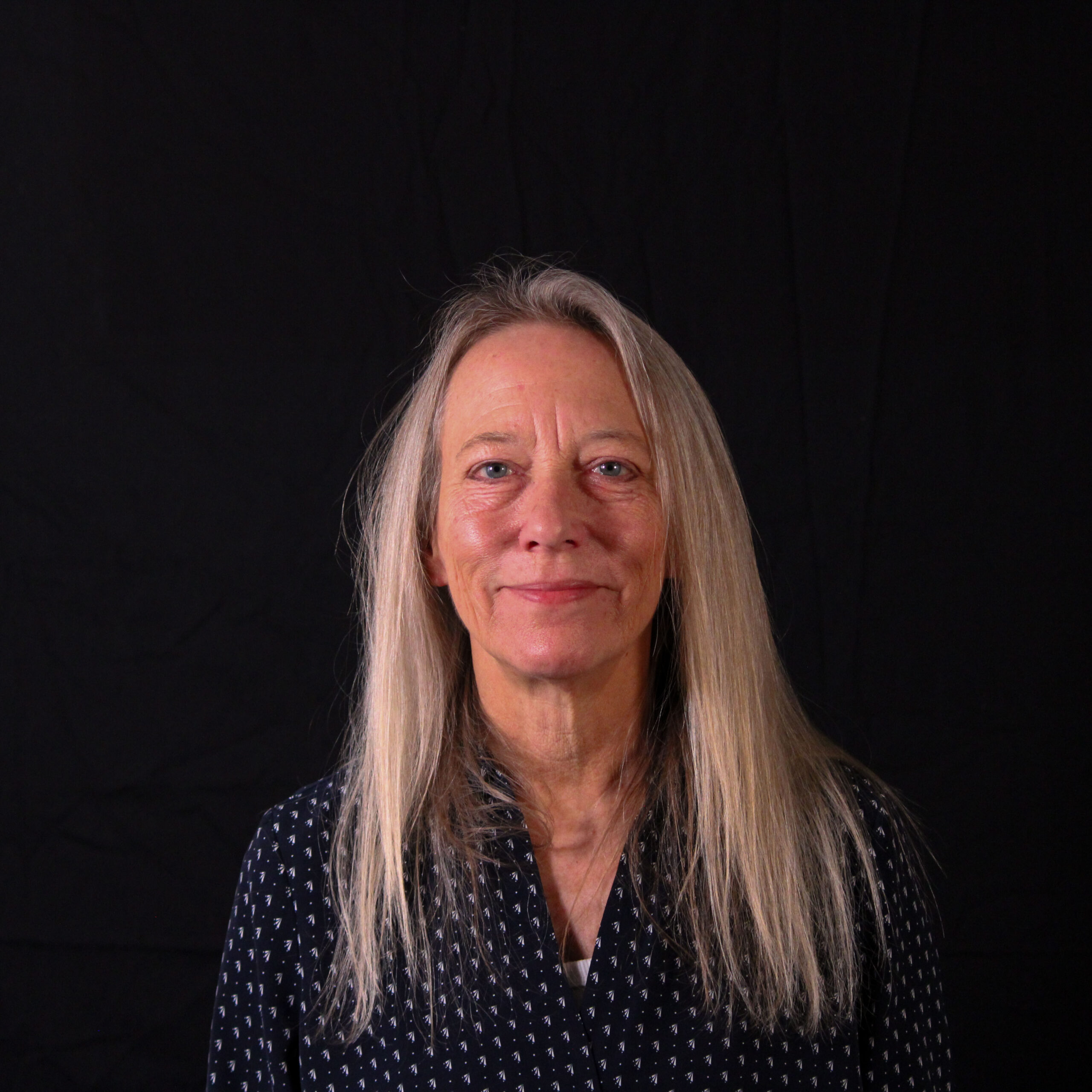 A woman smiling, dressed in a black shirt, against a black background.