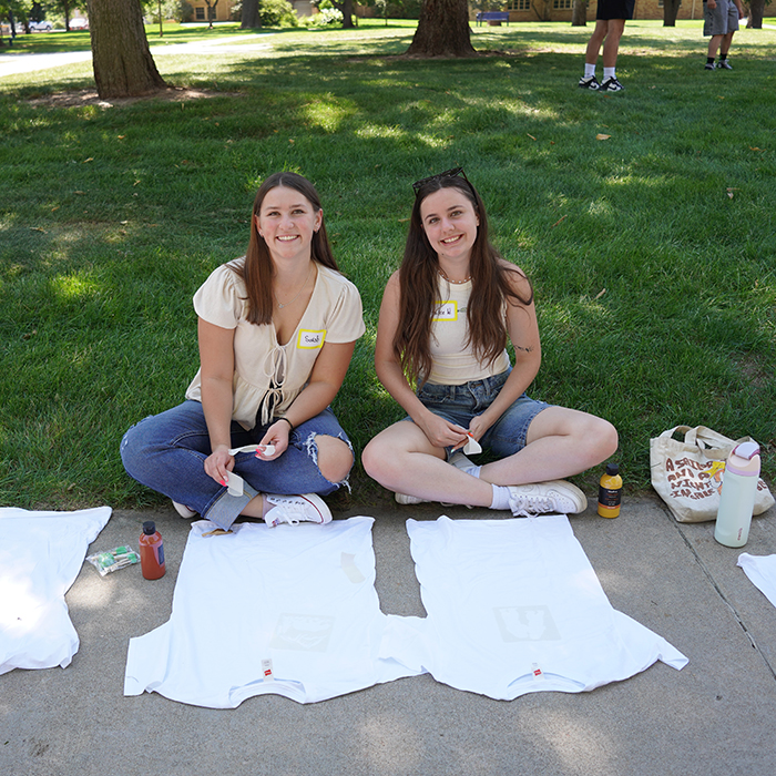 Two people sitting on the grass, working on a t-shirt painting activity outdoors.
