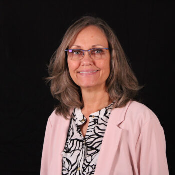 A woman smiling, dressed in a pink sweater, against a black background