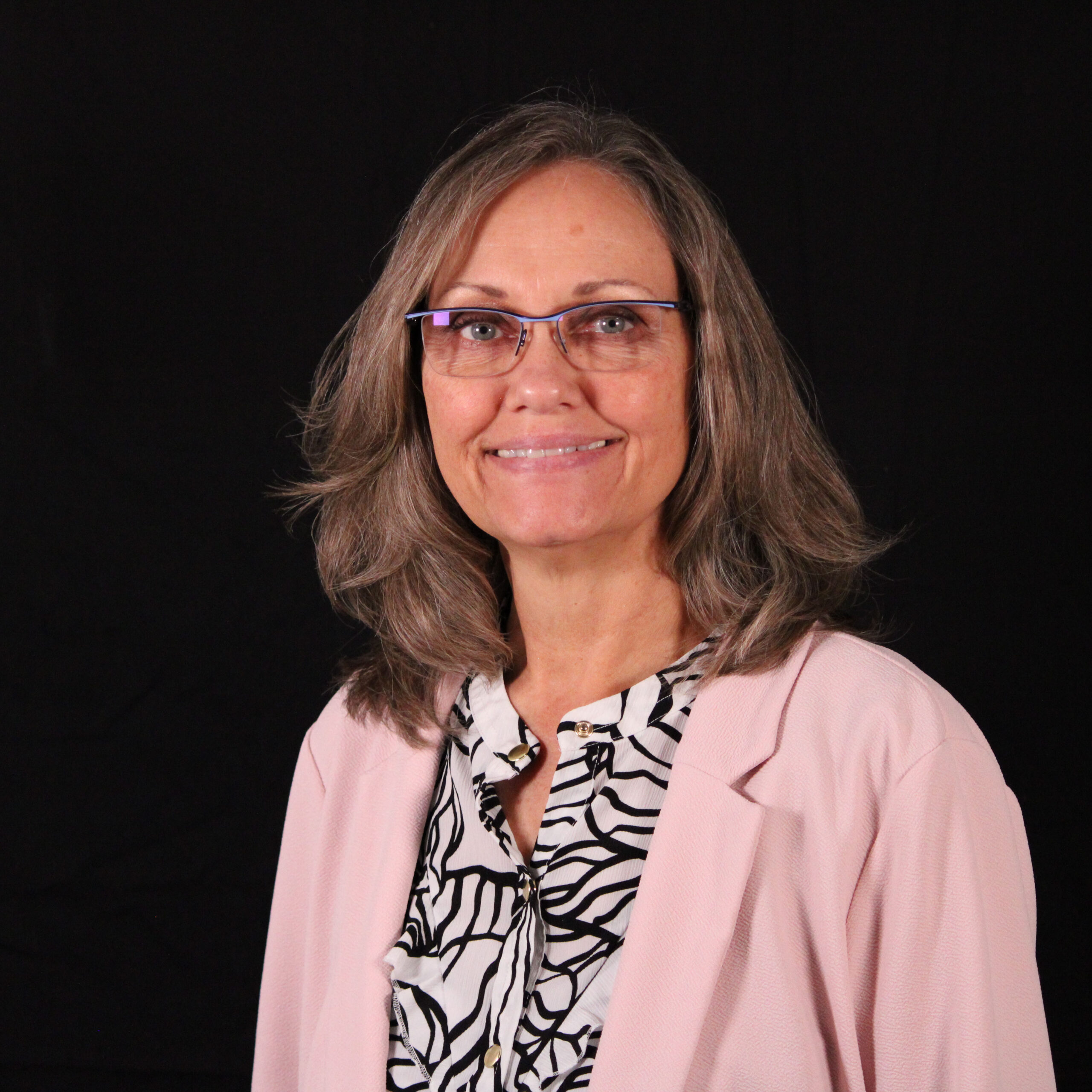 A woman smiling, dressed in a pink sweater, against a black background