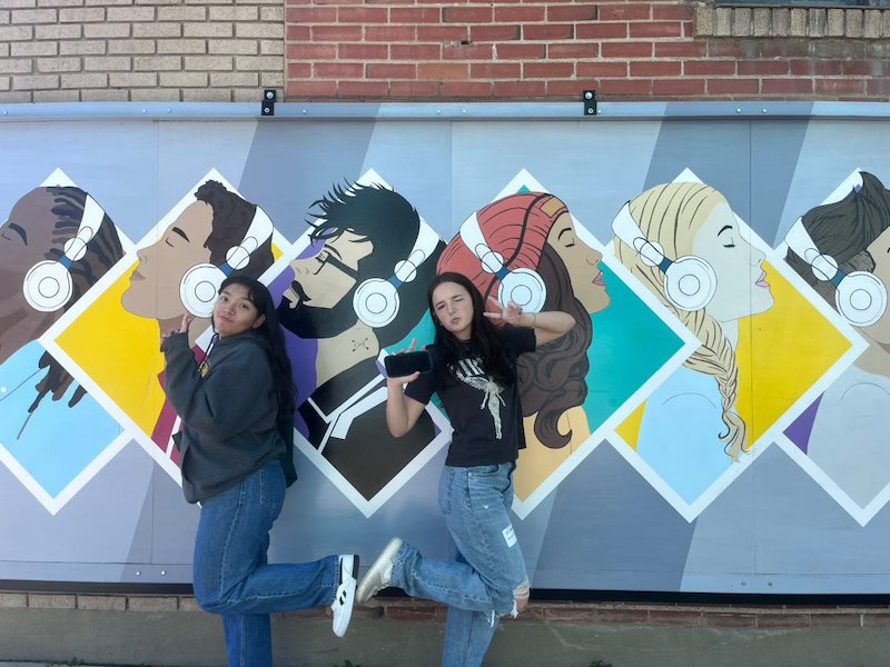 Two students dancing in front of a mural.