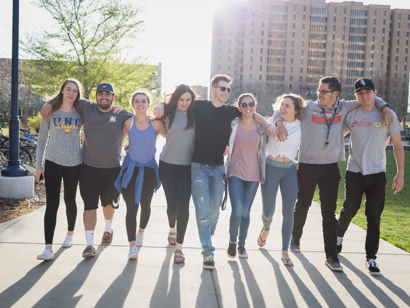 Students walking arm in arm on west campus with the sun setting behind them