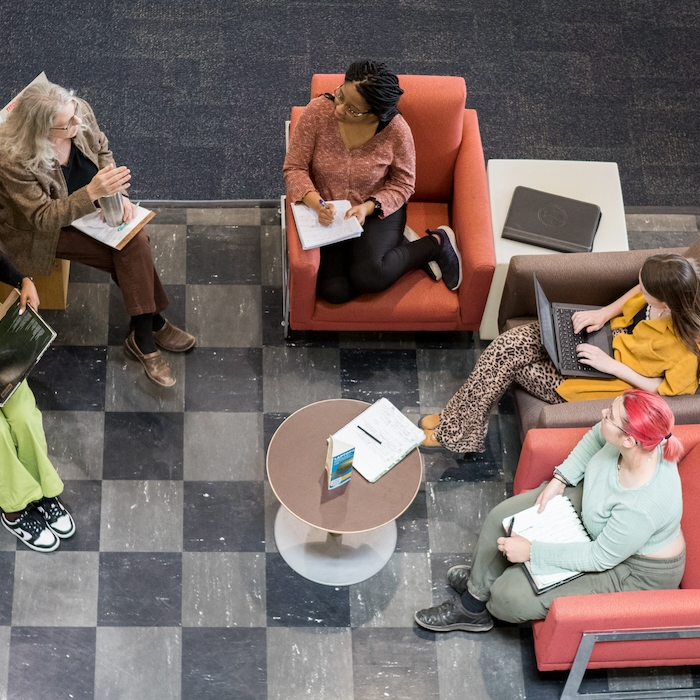 Students conversing with professor in a grouping of chairs as seen from above.