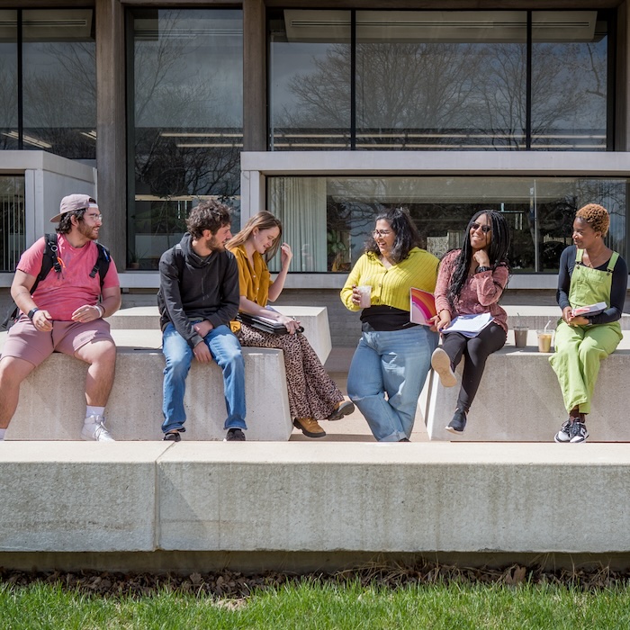 Group of students sitting outside of library with coffee drinks and chatting.