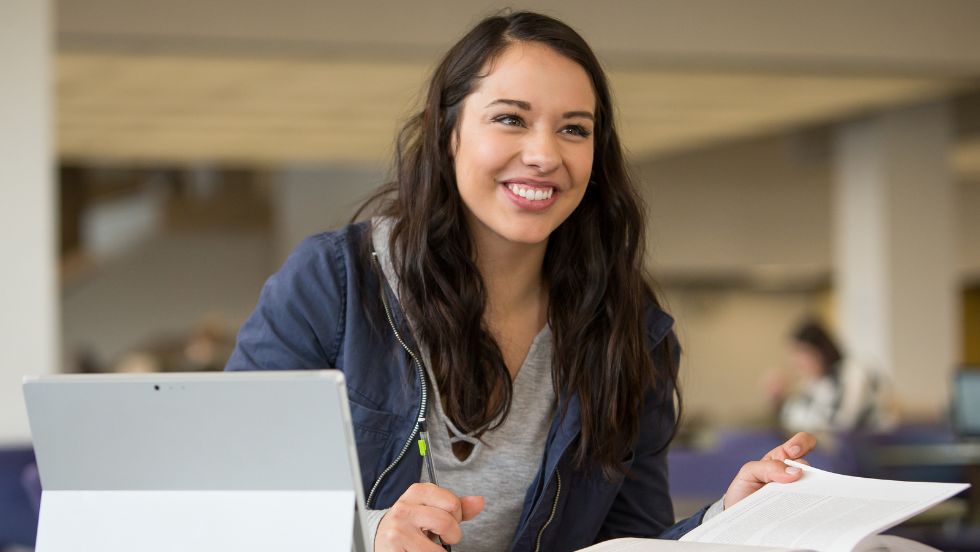 A student smiles as they work on their laptop in Michener Library