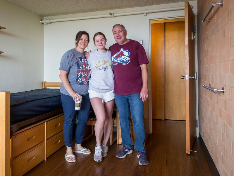 A student poses for a photo with her parents in her room at move-in day